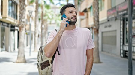 Téléchargez les photos : Jeune homme hispanique parlant sur smartphone portant un sac à dos dans la rue - en image libre de droit