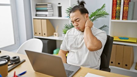 Photo for Stressed young chinese business worker battling cervical pain, glued to laptop at office - Royalty Free Image