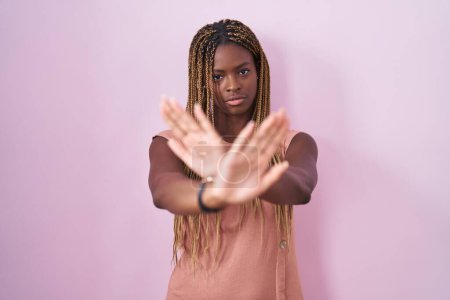 Photo for African american woman with braided hair standing over pink background rejection expression crossing arms and palms doing negative sign, angry face - Royalty Free Image