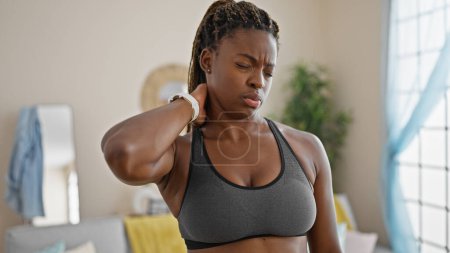 Foto de Mujer afroamericana usando ropa deportiva sufriendo por dolor cervical en casa - Imagen libre de derechos
