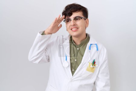 Téléchargez les photos : Jeune homme non binaire portant l'uniforme de médecin et stéthoscope très heureux et souriant regardant loin avec la main sur la tête. concept de recherche. - en image libre de droit