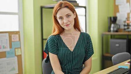 Téléchargez les photos : Jeune rousse femme d'affaires travailleur souriant confiant assis sur la table au bureau - en image libre de droit