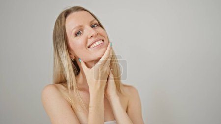Téléchargez les photos : Jeune femme blonde souriant visage de massage confiant sur fond blanc isolé - en image libre de droit