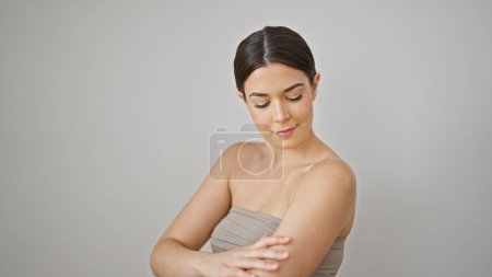 Téléchargez les photos : Jeune belle femme hispanique souriant confiant appliquer lotion sur le bras sur fond blanc isolé - en image libre de droit