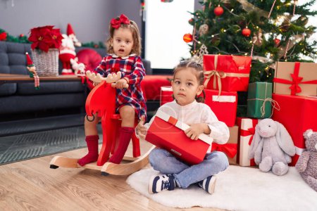 Foto de Hermano y hermana jugando con renos balanceo desembalaje regalo de Navidad en casa - Imagen libre de derechos