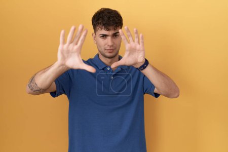 Photo for Young hispanic man standing over yellow background doing frame using hands palms and fingers, camera perspective - Royalty Free Image