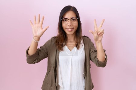 Foto de Mujer china de mediana edad con gafas sobre fondo rosa mostrando y apuntando hacia arriba con los dedos número ocho mientras sonríe confiado y feliz. - Imagen libre de derechos