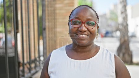 Téléchargez les photos : Femme afro-américaine confiante debout dans la rue urbaine, rayonnant de joie et de positivité, son rire contagieux répand le bonheur. ses tresses rebondissent, ses lunettes scintillent, sa vie vraiment aimante. - en image libre de droit