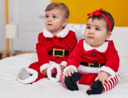 Téléchargez les photos : Adorable garçon et fille portant des vêtements de Noël assis sur le lit dans la chambre - en image libre de droit