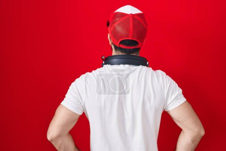 Foto de Hombre hispano con barba con sombrero de gamer y auriculares mirando hacia atrás con los brazos en el cuerpo - Imagen libre de derechos
