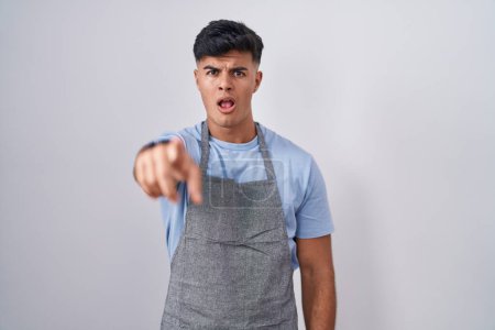 Photo for Hispanic young man wearing apron over white background pointing displeased and frustrated to the camera, angry and furious with you - Royalty Free Image