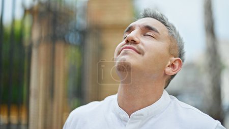 Téléchargez les photos : Jeune homme hispanique respirant les yeux fermés dans la rue - en image libre de droit