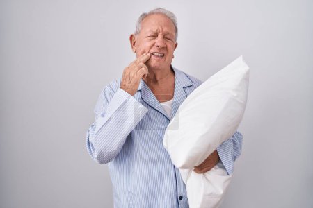 Photo for Senior man with grey hair wearing pijama hugging pillow touching mouth with hand with painful expression because of toothache or dental illness on teeth. dentist concept. - Royalty Free Image
