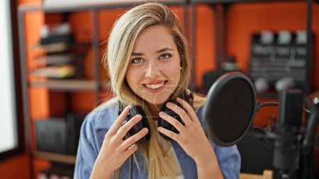 Téléchargez les photos : Jeune femme blonde musicienne souriante confiante portant des écouteurs au studio de musique - en image libre de droit
