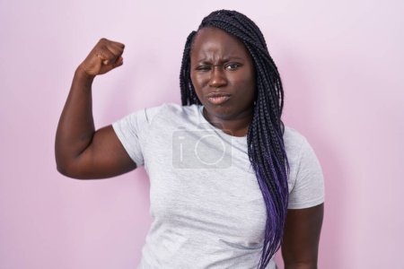 Foto de Mujer africana joven de pie sobre fondo rosa fuerte persona mostrando el músculo del brazo, confiado y orgulloso de poder - Imagen libre de derechos