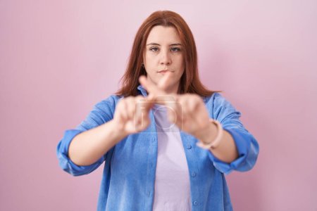 Téléchargez les photos : Jeune femme hispanique aux cheveux roux debout sur fond rose expression de rejet en croisant les doigts faisant signe négatif - en image libre de droit