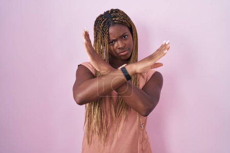 Téléchargez les photos : Femme afro-américaine avec des cheveux tressés debout sur fond rose expression de rejet croisant les bras faisant signe négatif, visage en colère - en image libre de droit