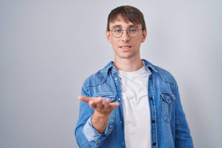 Photo for Caucasian blond man standing wearing glasses smiling cheerful offering palm hand giving assistance and acceptance. - Royalty Free Image