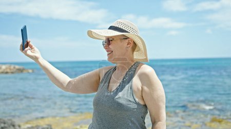 Photo for Middle age grey-haired woman tourist smiling confident make photo by smartphone at the beach - Royalty Free Image