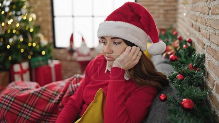 Téléchargez les photos : Jeune femme hispanique célébrant Noël avec une expression triste à la maison - en image libre de droit