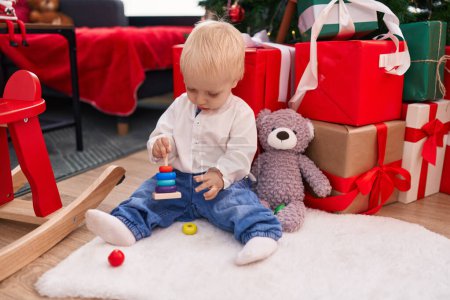 Téléchargez les photos : Adorable bambin blond jouant avec des jouets assis sur le sol par des cadeaux de Noël à la maison - en image libre de droit