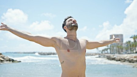 Foto de Joven turista hispano con traje de baño respirando con los brazos abiertos en la playa - Imagen libre de derechos