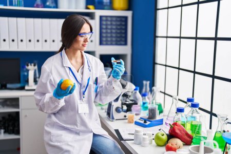 Téléchargez les photos : Jeune belle femme hispanique scientifique tenant du citron et des pilules au laboratoire - en image libre de droit
