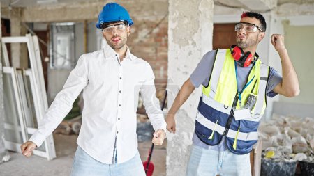 Foto de Dos hombres constructor y arquitecto sonriendo confiado bailando en el sitio de construcción - Imagen libre de derechos