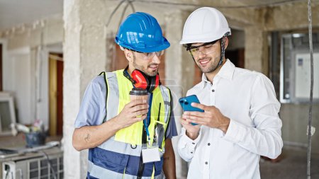 Photo for Two men builder and architect using smartphone drinking coffee at construction site - Royalty Free Image