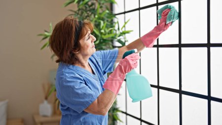 Foto de Mujer de mediana edad limpiador profesional ventana de lavado a casa - Imagen libre de derechos