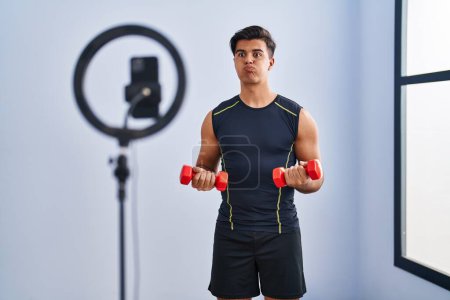 Téléchargez les photos : Hispanique homme enregistrement tutoriel d'entraînement à la salle de gym joues gonflées avec drôle de visage. bouche gonflée d'air, attrapant l'air. - en image libre de droit