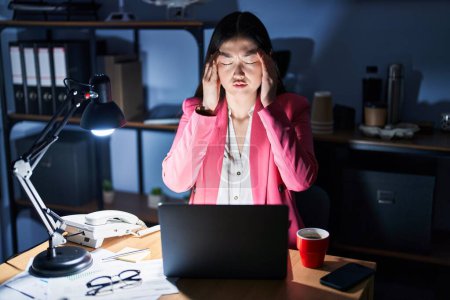 Photo for Chinese young woman working at the office at night with hand on head for pain in head because stress. suffering migraine. - Royalty Free Image