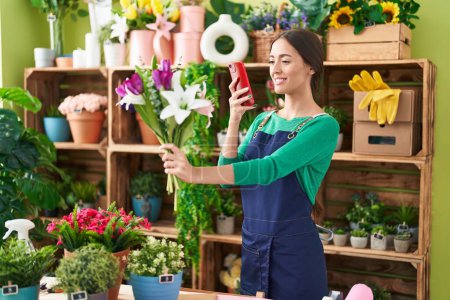 Foto de Joven florista hermosa mujer hispana hacer foto para florecer por teléfono inteligente en la tienda de flores - Imagen libre de derechos