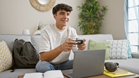 Photo for Hispanic teenager having a blast, young student smiles away while comfortably seated on sofa, engrossed in his favorite video game at home - Royalty Free Image