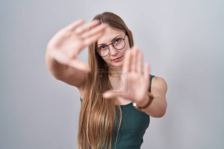 Foto de Joven mujer caucásica de pie sobre fondo blanco haciendo marco usando las manos palmas y los dedos, perspectiva de la cámara - Imagen libre de derechos