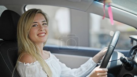 Foto de Joven mujer rubia sonriendo seguro de conducir coche en la calle - Imagen libre de derechos