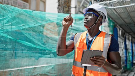 Foto de Hombre afroamericano constructor usando touchpad mirando alrededor en el lugar de construcción - Imagen libre de derechos