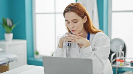Téléchargez les photos : Jeune rousse femme médecin en utilisant un ordinateur portable à la clinique - en image libre de droit