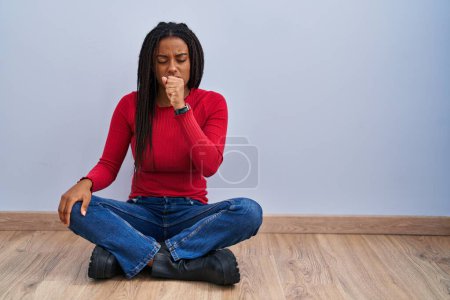 Photo for Young african american with braids sitting on the floor at home feeling unwell and coughing as symptom for cold or bronchitis. health care concept. - Royalty Free Image