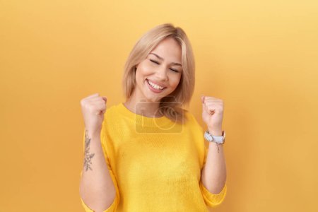 Photo for Young caucasian woman wearing yellow sweater very happy and excited doing winner gesture with arms raised, smiling and screaming for success. celebration concept. - Royalty Free Image
