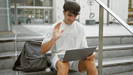 Photo for Caught in the moment, smiling, handsome young hispanic teenager taking break on university stairs, juggling student life, sunlit casual lifestyle and online education through cool video call - Royalty Free Image
