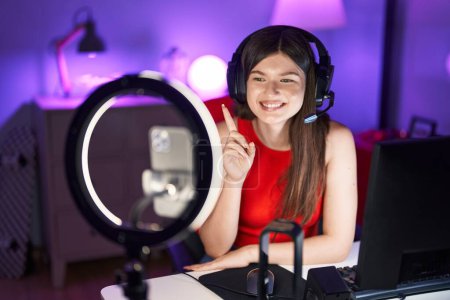 Téléchargez les photos : Jeune femme caucasienne jouant à des jeux vidéo enregistrement avec smartphone souriant heureux pointant avec la main et le doigt sur le côté - en image libre de droit