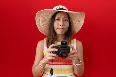 Téléchargez les photos : Femme chinoise du Moyen Age utilisant un appareil photo réflexe portant un chapeau d'été sceptique et nerveux, fronçant les sourcils bouleversés en raison de problèmes. personne négative. - en image libre de droit