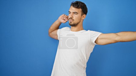 Foto de Hombre hispano joven extendiendo brazos sobre fondo azul aislado - Imagen libre de derechos