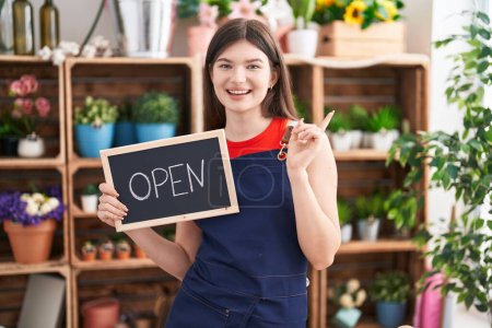 Photo for Young caucasian woman working at florist holding open sign smiling happy pointing with hand and finger to the side - Royalty Free Image