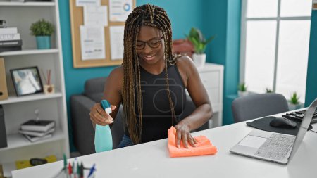 Foto de Trabajadora de negocios afroamericana limpiando mesa sonriendo en la oficina - Imagen libre de derechos