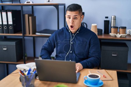 Photo for Hispanic young man working at the office with laptop scared and amazed with open mouth for surprise, disbelief face - Royalty Free Image