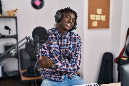 Foto de Afro-americano músico sonriendo confiado sentado con los brazos cruzados gesto en el estudio de música - Imagen libre de derechos