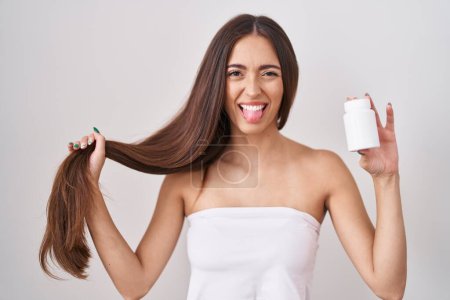 Téléchargez les photos : Jeune femme hispanique tenant les cheveux avec la main et les pilules collant la langue heureux avec une expression drôle. - en image libre de droit