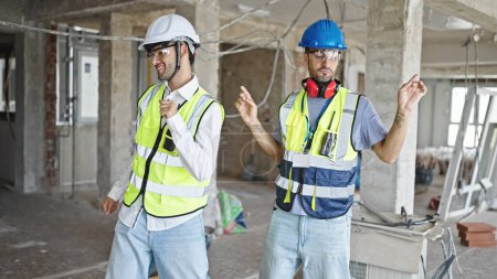 Téléchargez les photos : Deux hommes constructeurs souriant danse confiante sur le chantier de construction - en image libre de droit